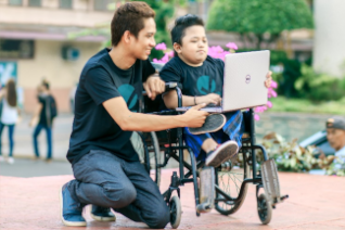 A person teaching another person in a wheelchair using a laptop
