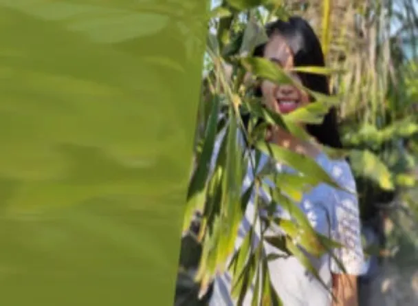 A woman hiding behind a branch full of green leaves