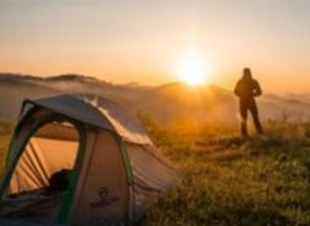 A man facing the sunrise beside his tent