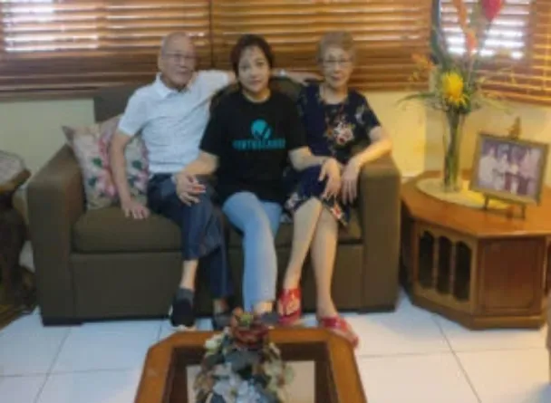 Monique Fojias sitting with her parents on a couch